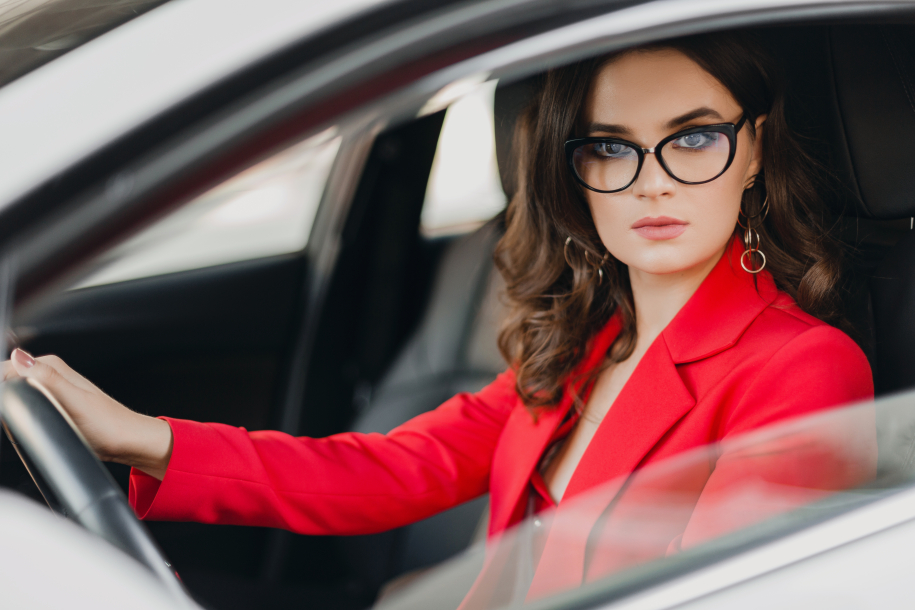 business woman in red suit sitting in white car, wearing glasses