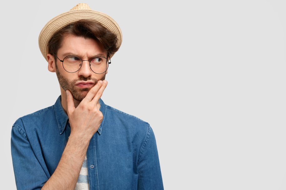 Serious thoughtful male farmer holds chin, thinks how to succeed in agricultural sphere, dressed in stylish straw hat and casual shirt, stands against white background with copy space for your text