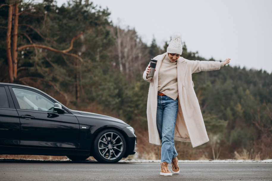 Woman drinking coffee by her car standing on the road in forest