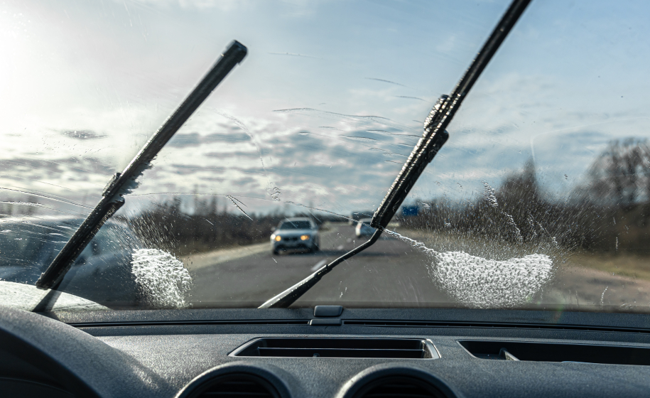 Car wipers clean windshields when driving in sunny weather, inside view.