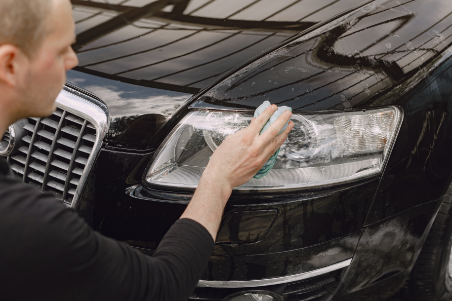 Man in a black sweater. Worker wipes a car. Male holding a rag in his hand.