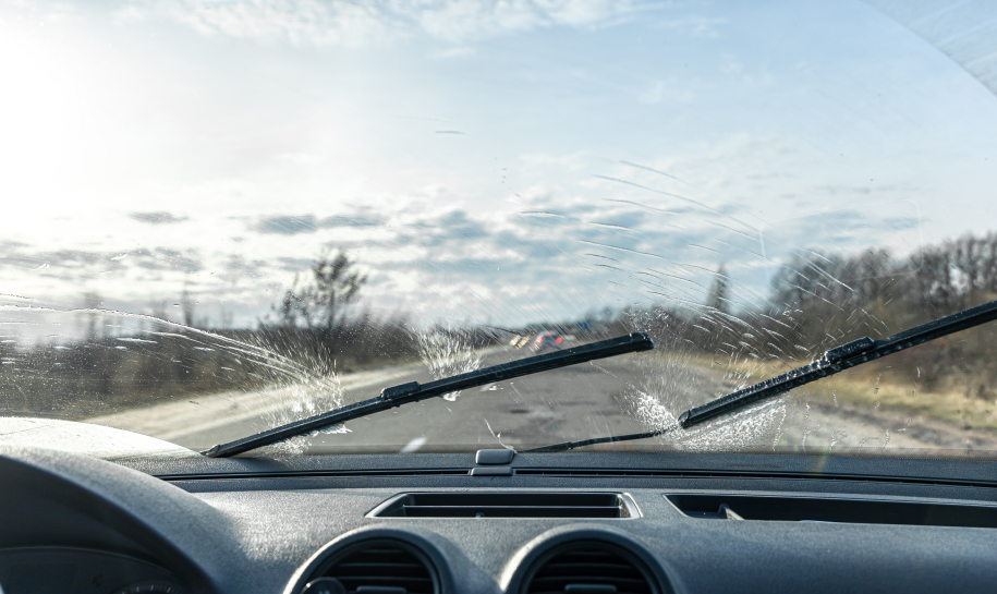 Car wipers clean windshields when driving in sunny weather, inside view.