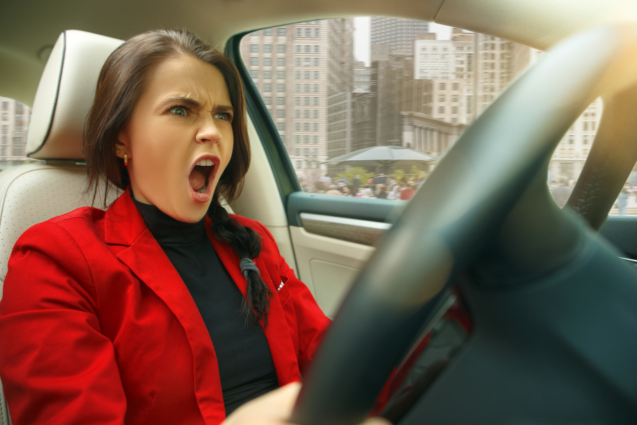 Driving and stress. Young attractive woman driving a car. Screaming surprised caucasian model in elegant stylish red jacket sitting at modern vehicle interior. Businesswoman concept. Human emotions concepts