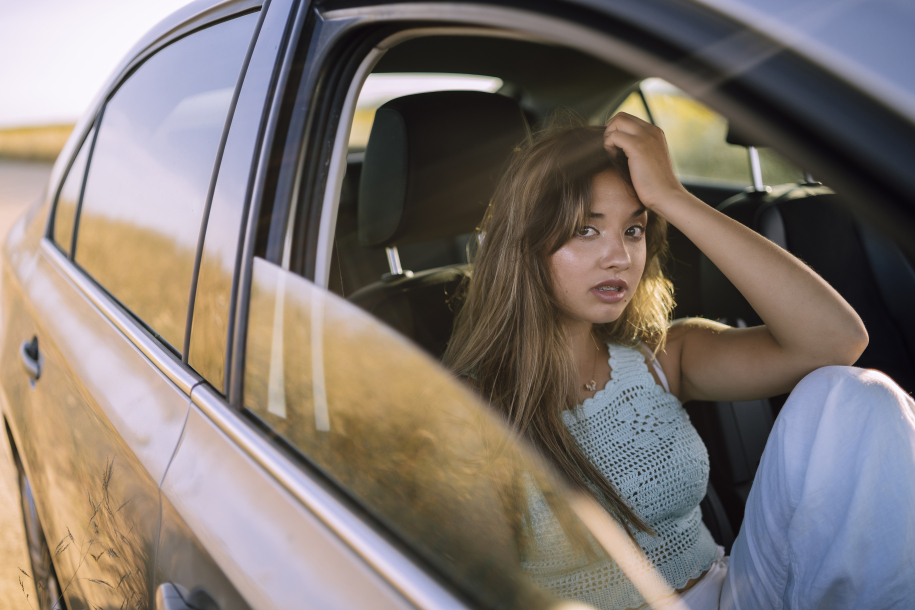 A horizontal shot of a beautiful young caucasian female posing in the front seat of a car in a field